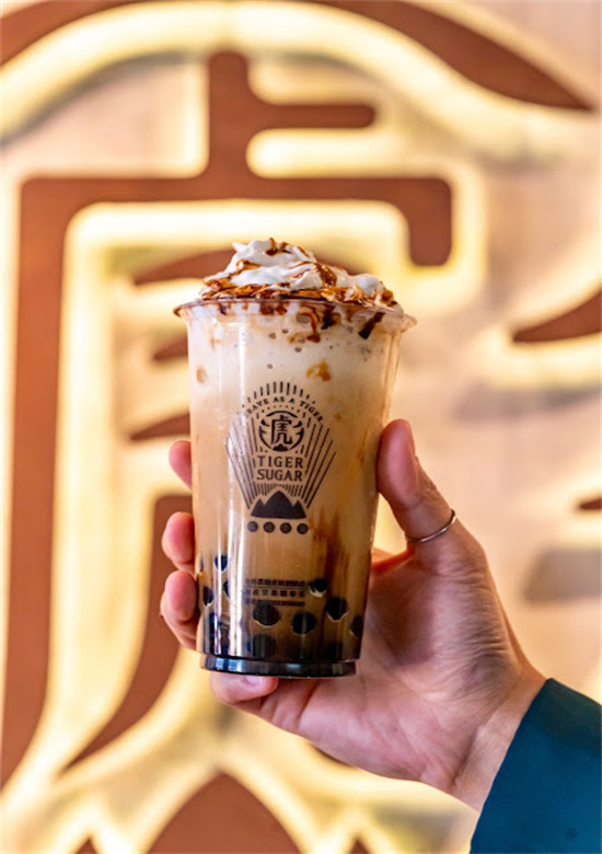Hand holding creamy boba drink topped with whipped cream against store signage at Tiger Sugar, a Bubble tea store in Philadelphia