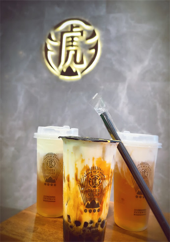 Three bubble tea cups placed beneath glowing Tiger Sugar logo at Tiger Sugar, a Bubble tea store in Philadelphia
