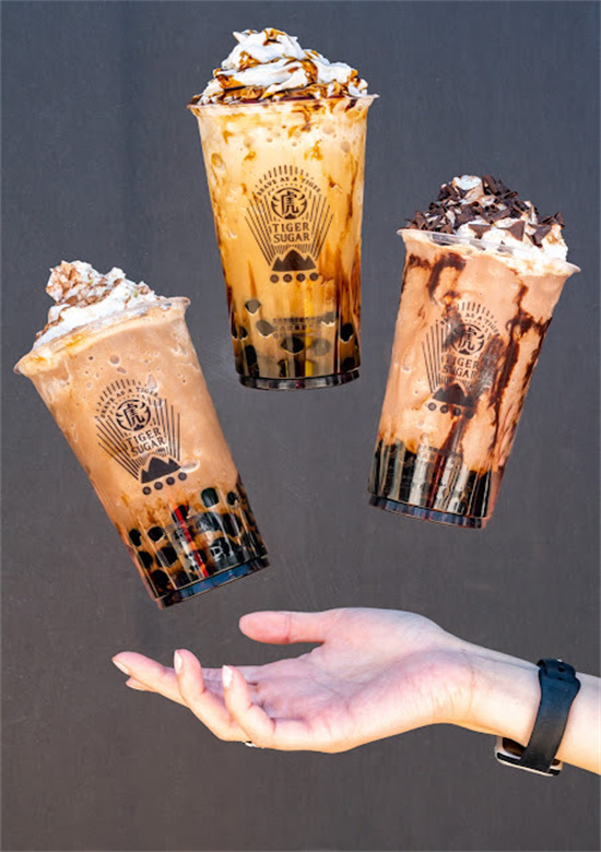 Three floating decorated bubble tea cups above an open palm at Tiger Sugar, a Bubble tea store in Philadelphia