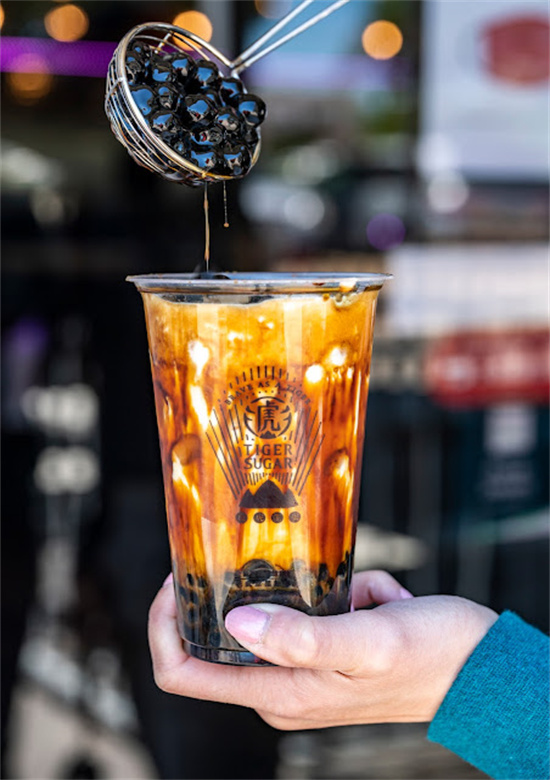 Hand holding bubble tea as tapioca drips from metal strainer at Tiger Sugar, a Bubble tea store in Philadelphia