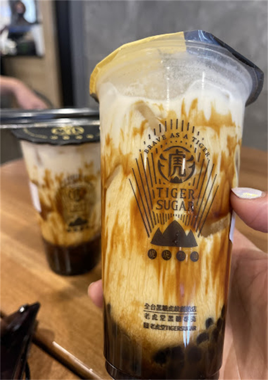 Hand holding plastic cup of brown sugar boba milk tea with tiger stripe syrup at Tiger Sugar, a Bubble tea store in Philadelphia