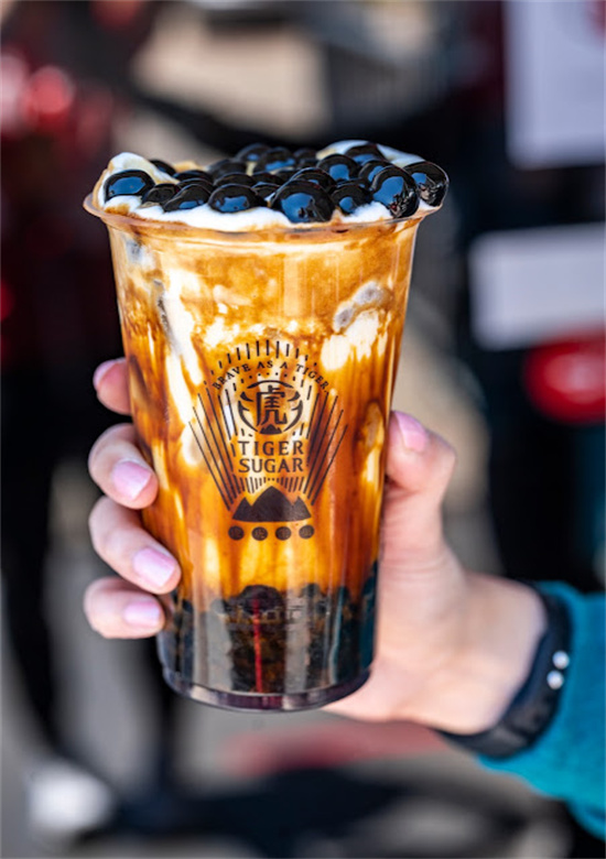 Hand gripping Tiger Sugar cup filled with brown sugar boba milk tea and pearls at Tiger Sugar, a Bubble tea store in Philadelphia