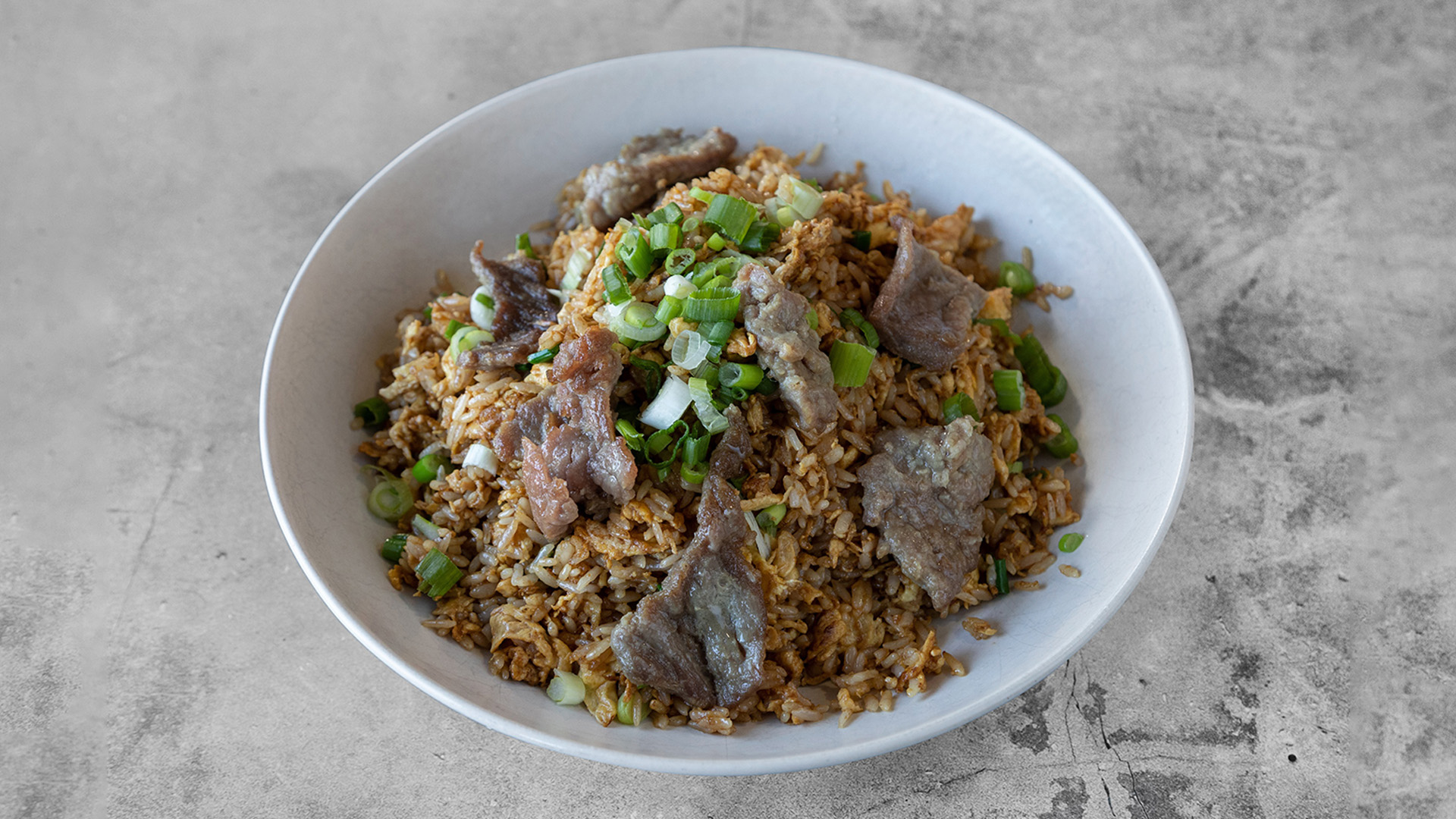 Beef fried rice topped with sliced beef and chopped green onions in plain white ceramic bowl at Mandarin Chinese & Japanese Cuisine , a Chinese Restaurant in Santa Monica