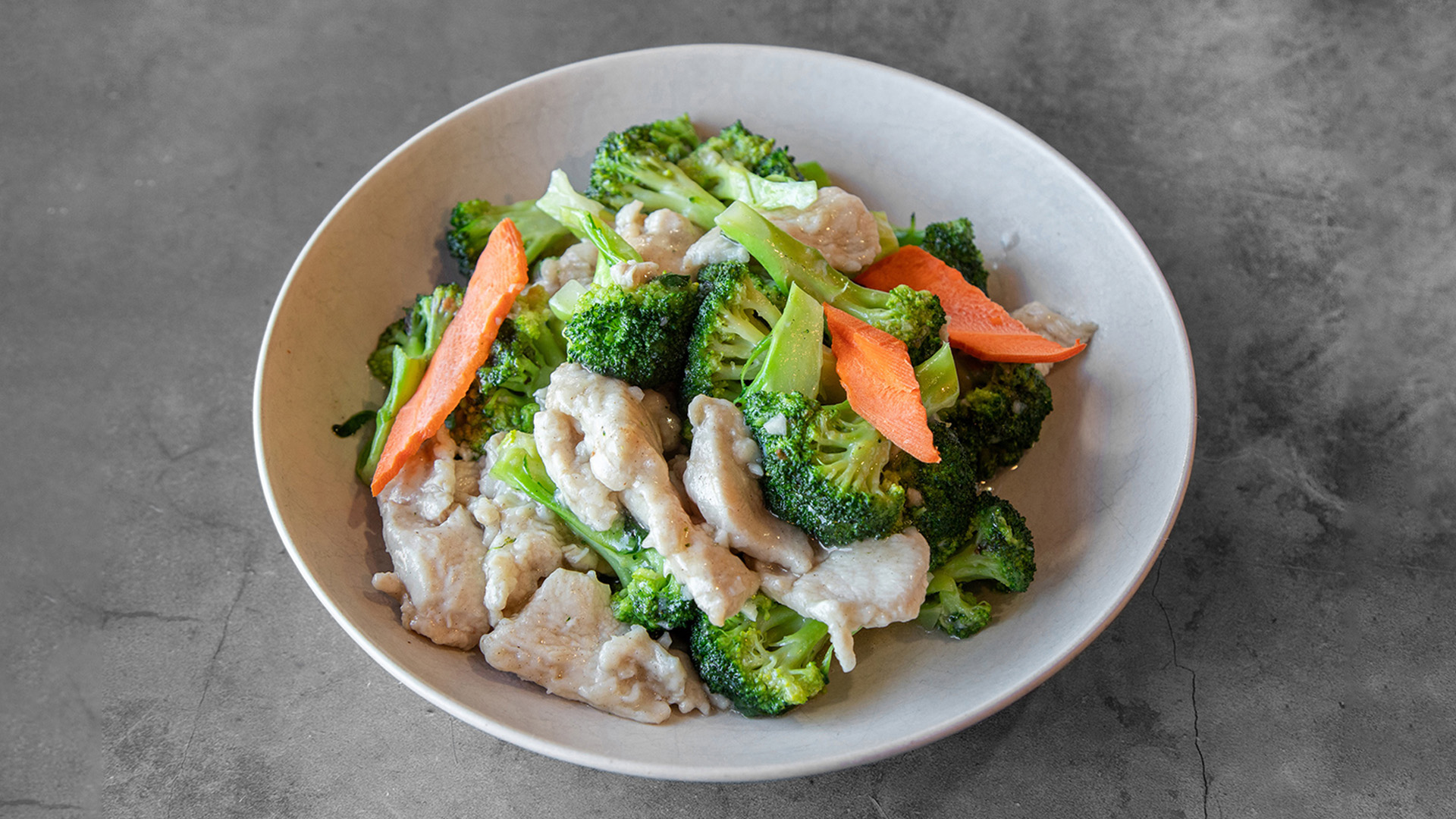 Lightly stir-fried chicken breast with fresh broccoli and orange carrot strips in creamy pale sauce in white bowl at Mandarin Chinese & Japanese Cuisine , a Chinese Restaurant in Santa Monica