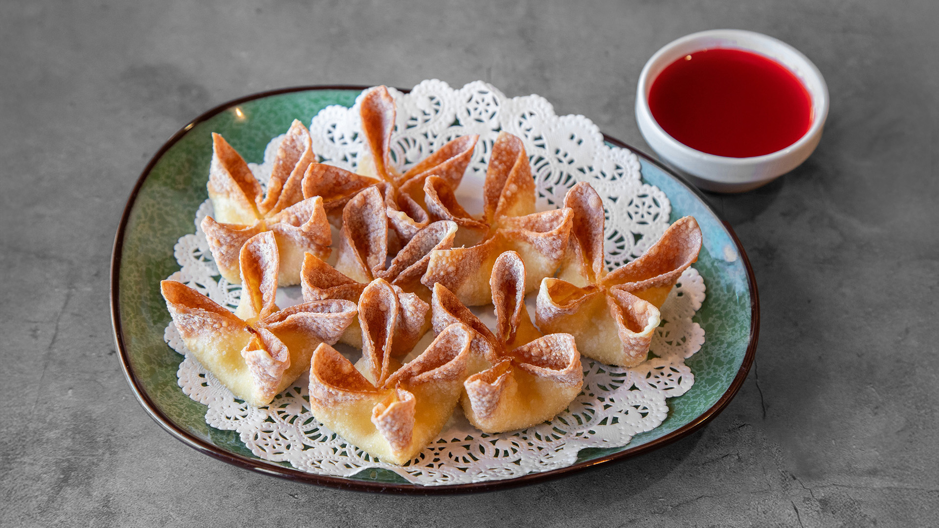 Crispy cream cheese wontons arranged on lace paper with small bowl of red sweet-and-sour dipping sauce on green plate at Mandarin Chinese & Japanese Cuisine , a Chinese Restaurant in Santa Monica