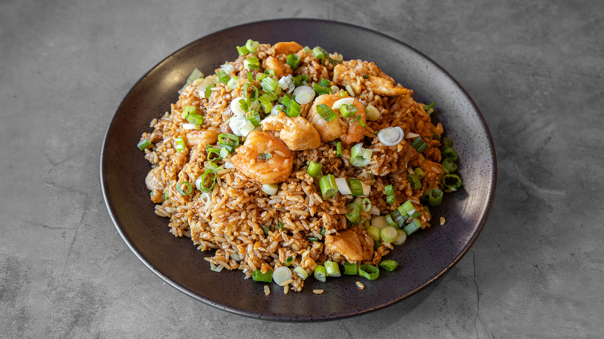 Combination seafood fried rice with plump shrimp, diced chicken and sliced scallions on dark round ceramic plate at Mandarin Chinese & Japanese Cuisine , a Chinese Restaurant in Santa Monica