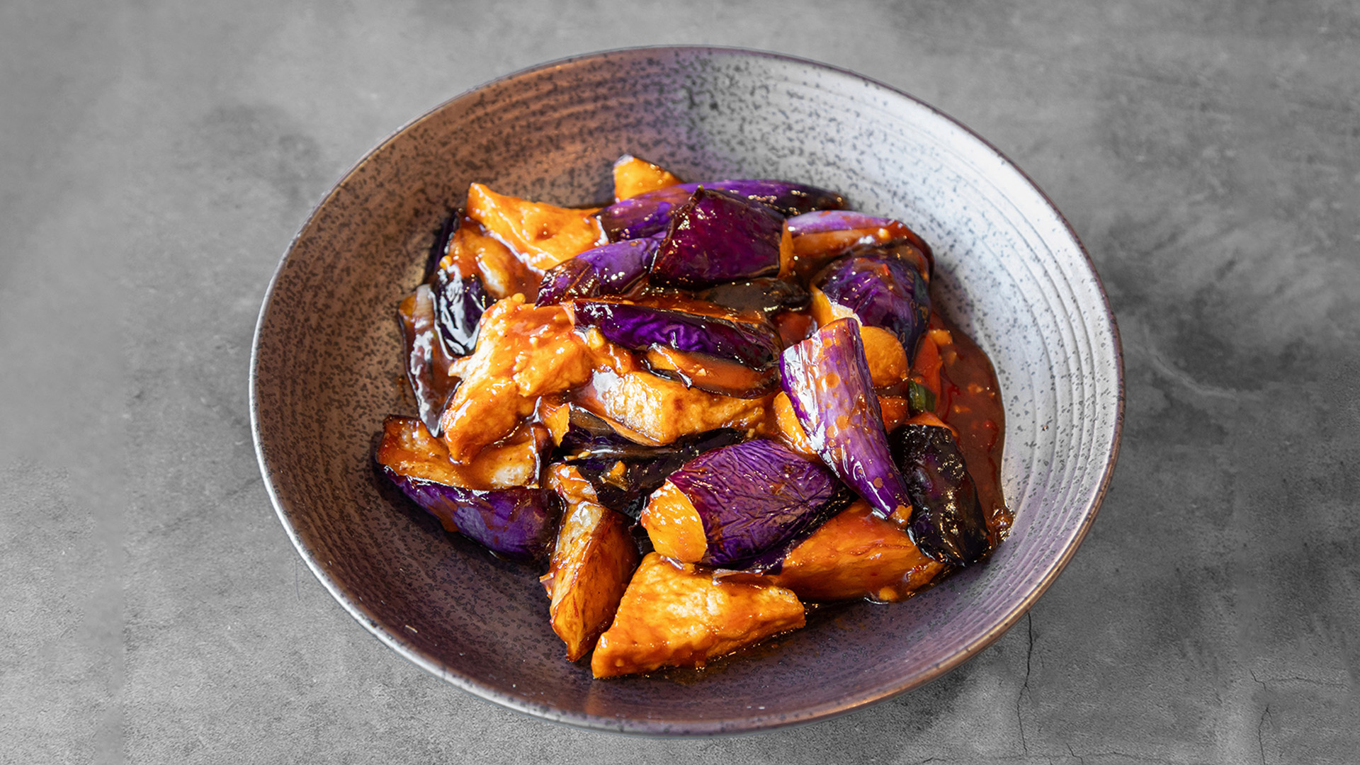 Braised eggplant and tofu chunks glazed in rich spicy reddish-brown sauce inside textured grey ceramic bowl at Mandarin Chinese & Japanese Cuisine , a Chinese Restaurant in Santa Monica