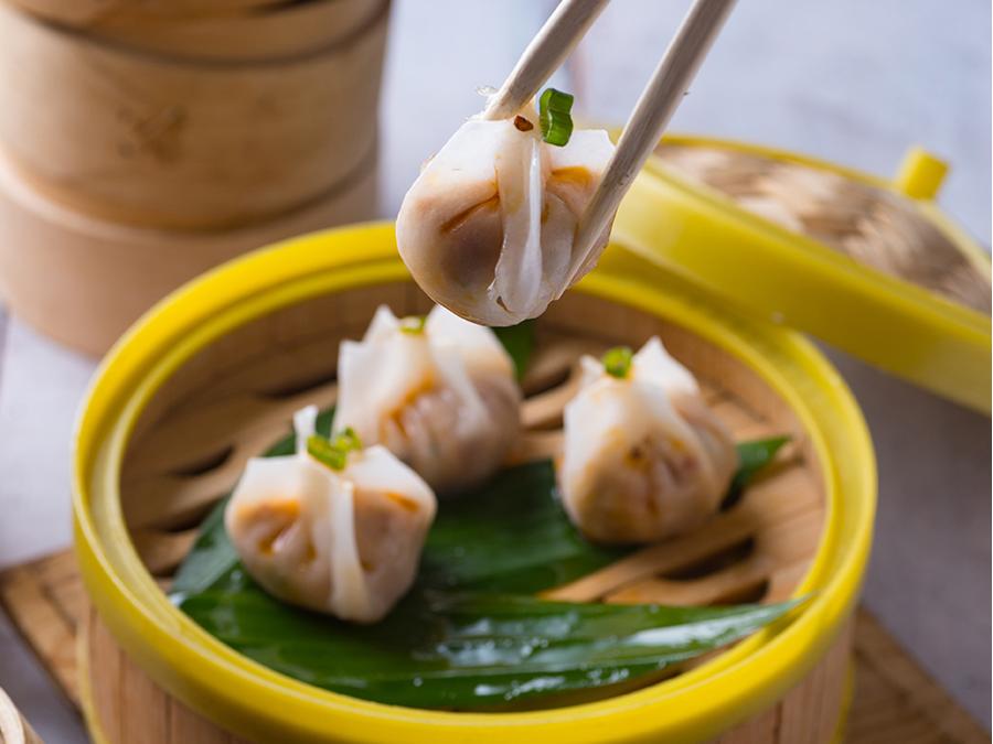 Delicate dim sum bites in a yellow steamer, picked with chopsticks at Tokyo Cafe Sushi and Asian Food, a Asian Fusion Restaurant in Lubbock