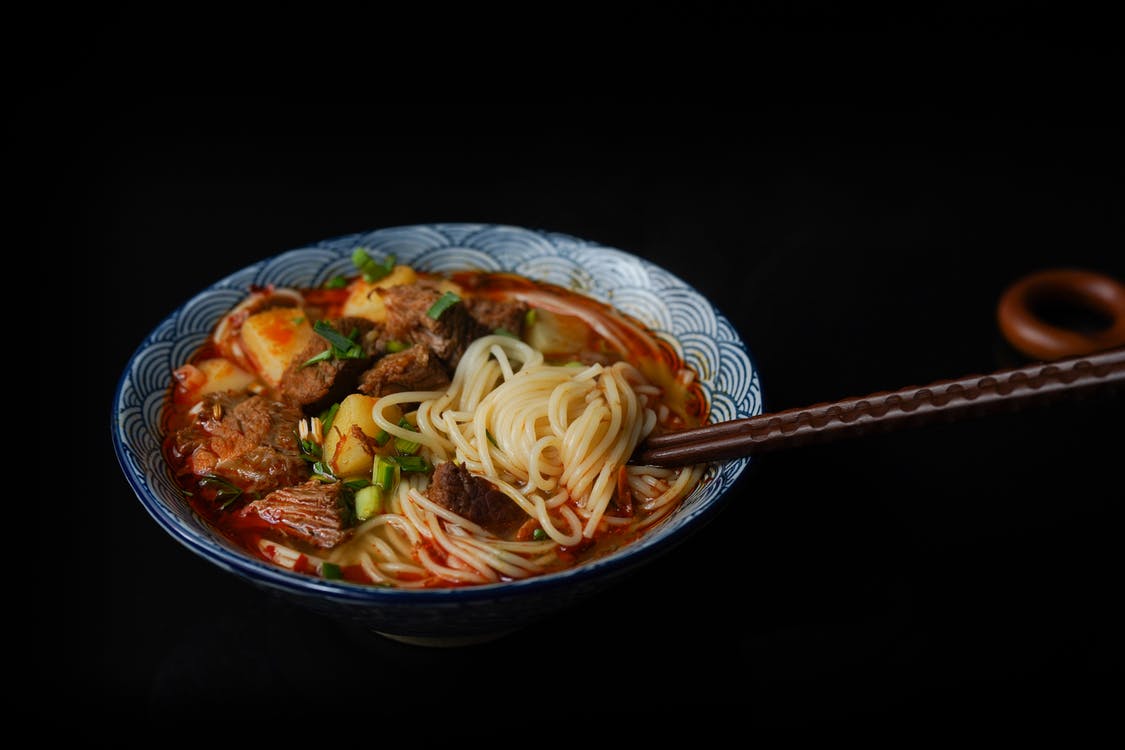 Bowl of spicy beef noodle soup with chopsticks, garnished with green onions
