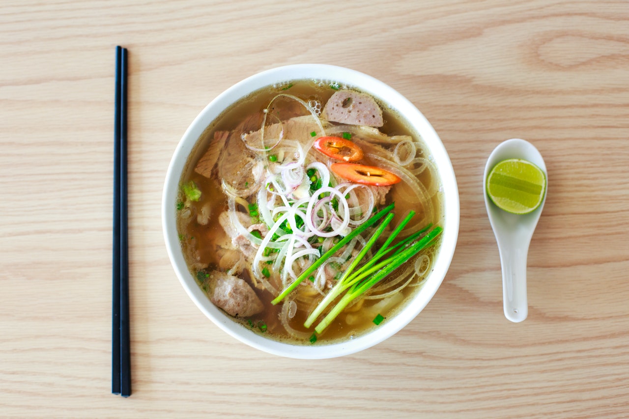 Bowl of pho soup with noodles, meat, herbs, and a side of lime and chopsticks