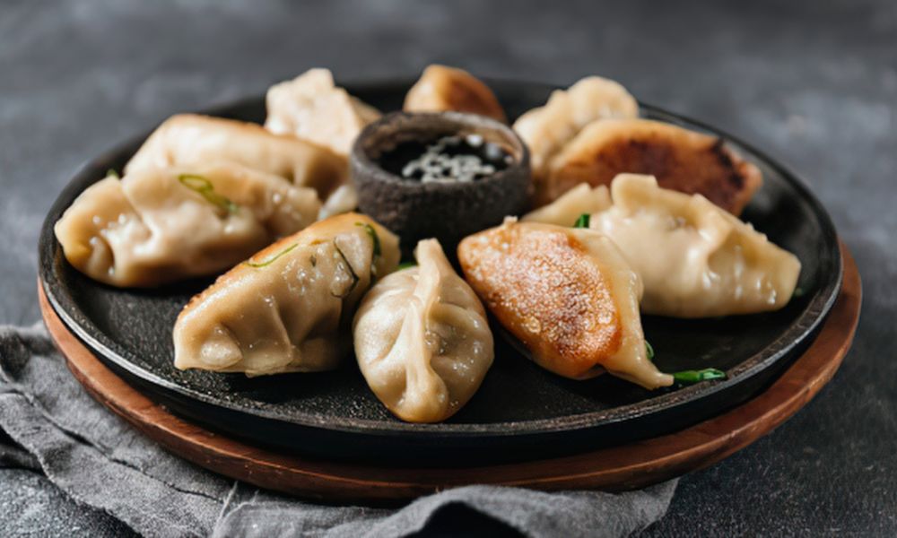 Mixed steamed and pan-fried dumplings with dipping sauce on a black plate at Toro 7 Sushi, a Sushi Restaurant in New York