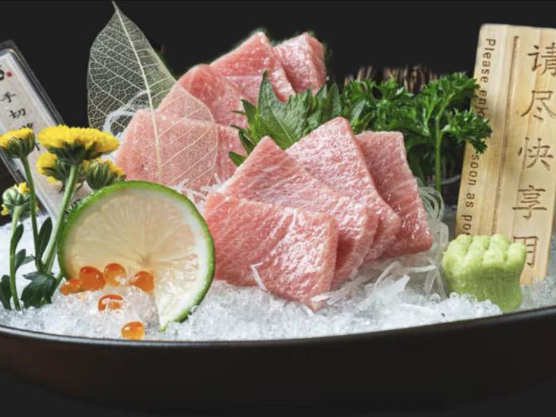 Plate of premium pink toro tuna sashimi served on crushed ice, garnished with lime, chrysanthemum flowers and fresh wasabi at Toromi Sushi , a Sushi Restaurant in West Covina
