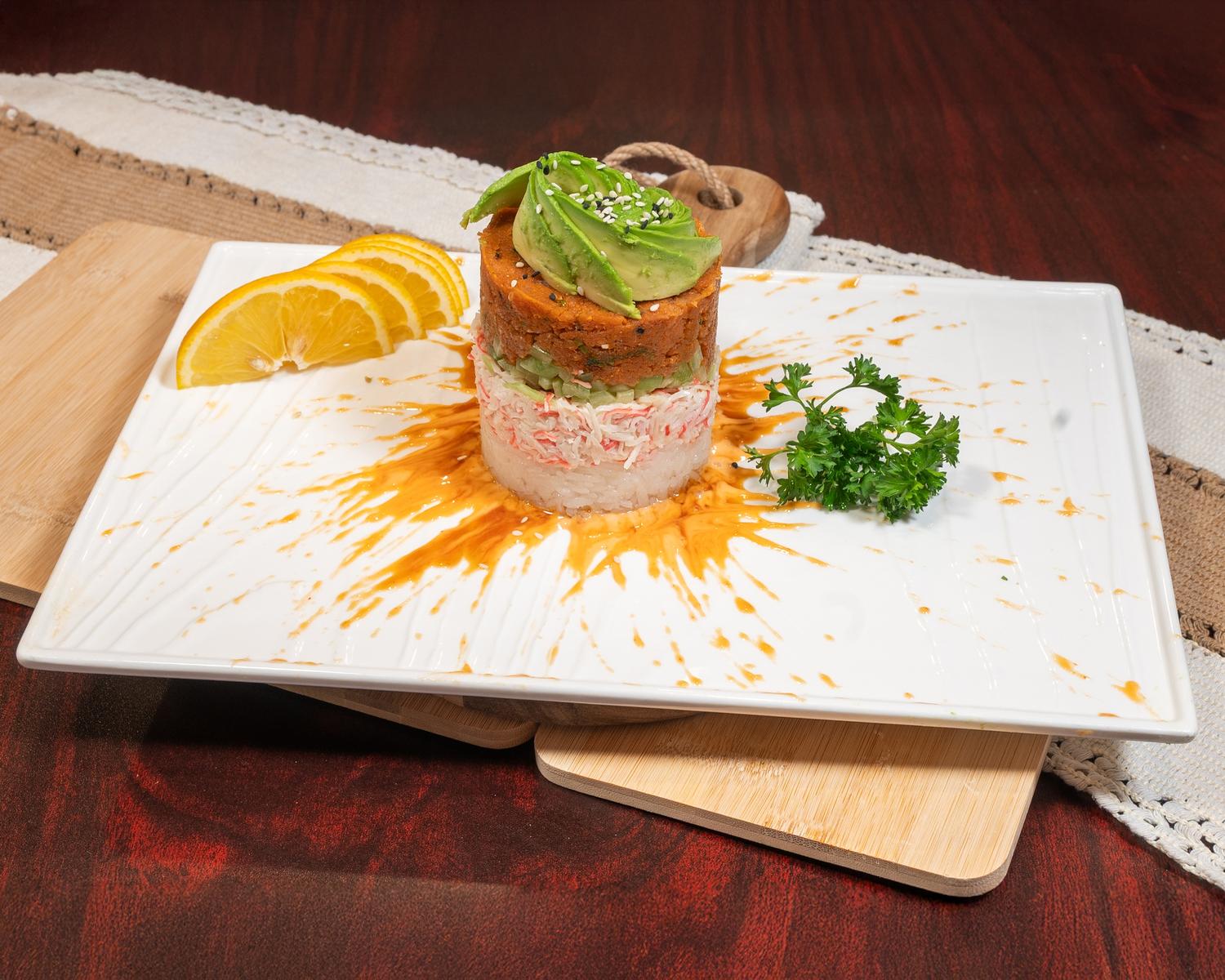 Layered seafood sushi stack with crab, spicy tuna, avocado and citrus garnish on ceramic plate at Ubin Sushi, a Japanese restaurant in Colorado Springs