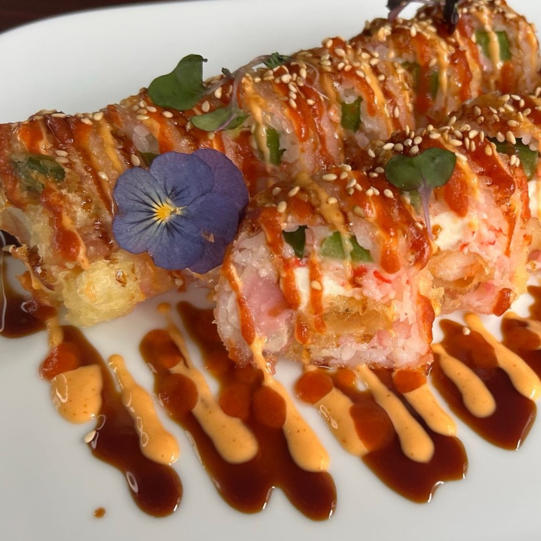Crispy tempura sushi roll drizzled with dual savory sauces and edible violet flower at Umami Sushi & Chinese Cuisine, an Asian Fusion Restaurant in Minneapolis