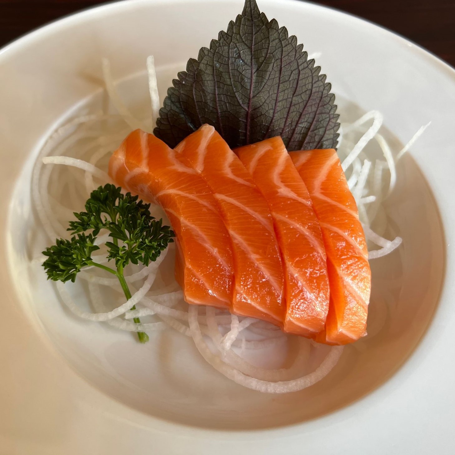 Fresh salmon sashimi slices served over shredded daikon radish with herb garnish at Umami Sushi & Chinese Cuisine, an Asian Fusion Restaurant in Minneapolis