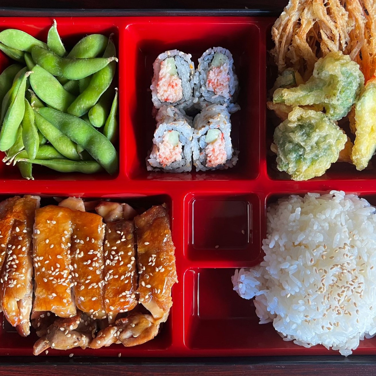 Six-compartment red bento box with teriyaki chicken, edamame, tempura and sushi rolls at Umami Sushi & Chinese Cuisine, an Asian Fusion Restaurant in Minneapolis