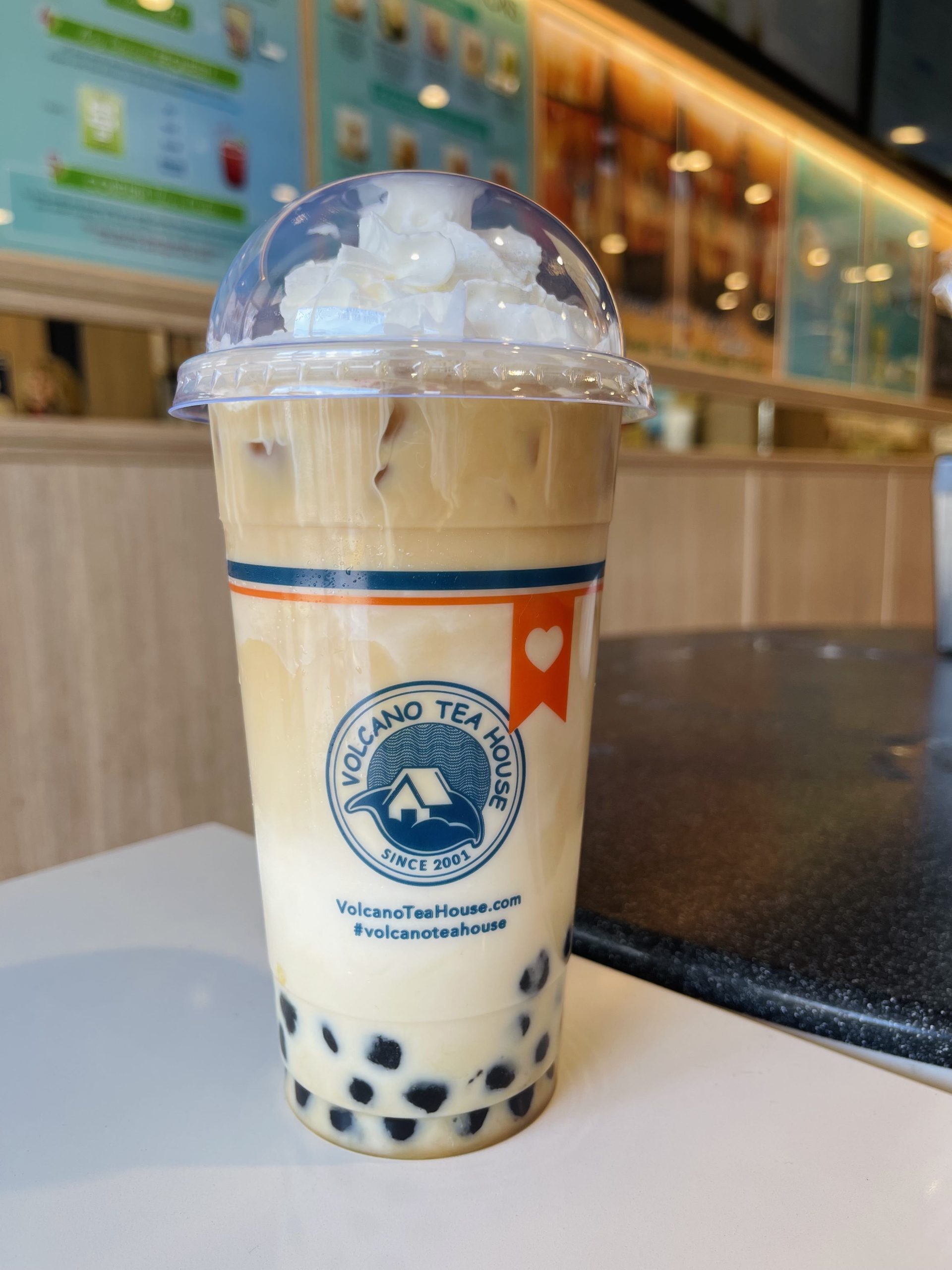 Plastic cup of bubble milk tea topped with whipped cream on counter at Volcano Tea House, a Bubble tea store in Los Angeles