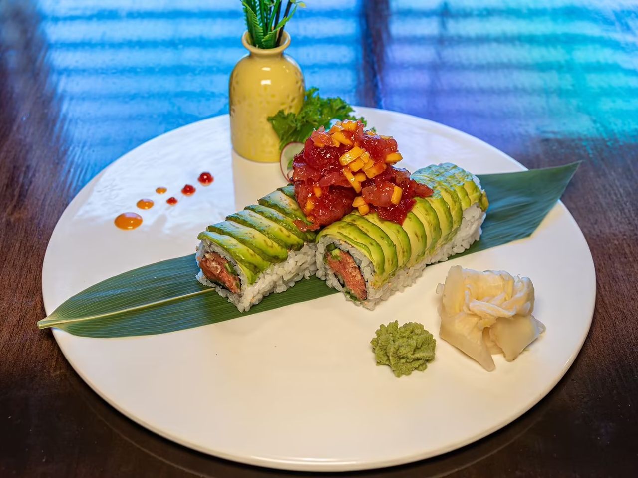 Avocado-topped sushi roll with spicy tuna, served with wasabi and pickled ginger