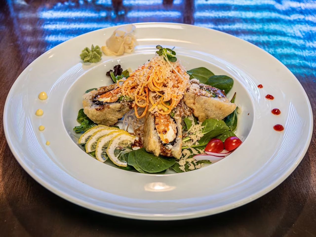 Crispy sushi rolls over greens with shredded toppings, lemon slices, ginger, and wasabi