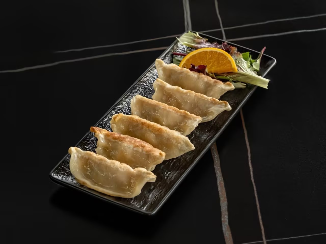 Pan-fried pot stickers served with mixed greens and an orange slice