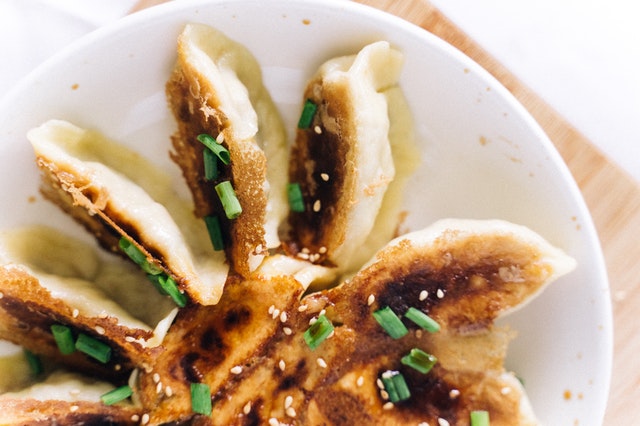 On the white plate, there are many fried dumplings with scallions sprinkled on top.