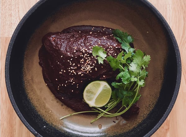 Mole chicken in a cast - iron pan, covered with rich mole sauce, paired with lime slices and cilantro