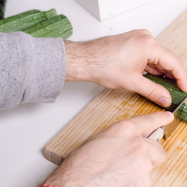 Hands cutting zucchini on a wooden cutting board