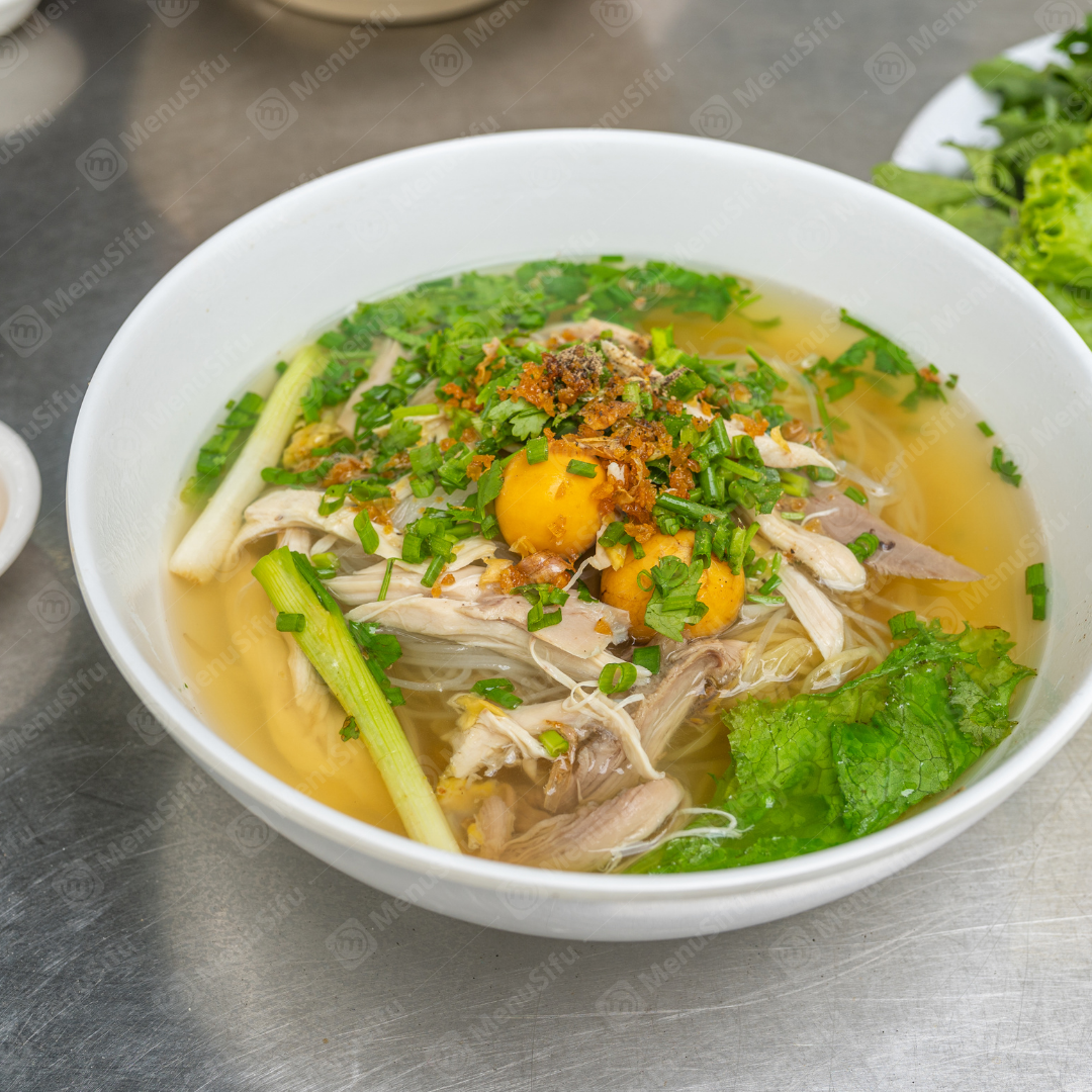 Chicken Noodle Soup is a comforting dish with tender shredded chicken, vermicelli noodles, and garnishes like scallions and herbs in a flavorful broth.