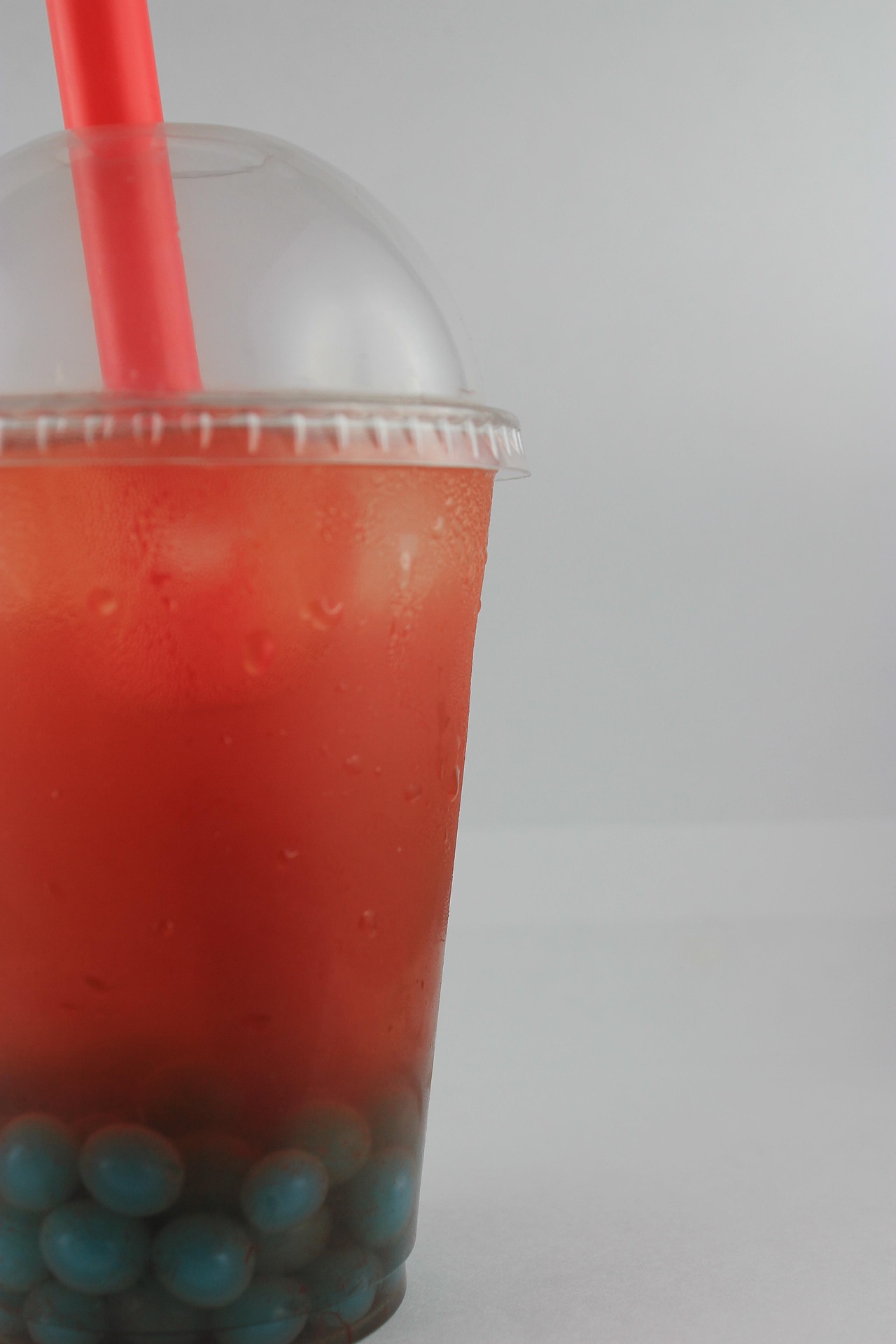 Close-up of a clear plastic cup containing red iced beverage with blue tapioca pearls at the bottom and a red straw inserted through the lid.