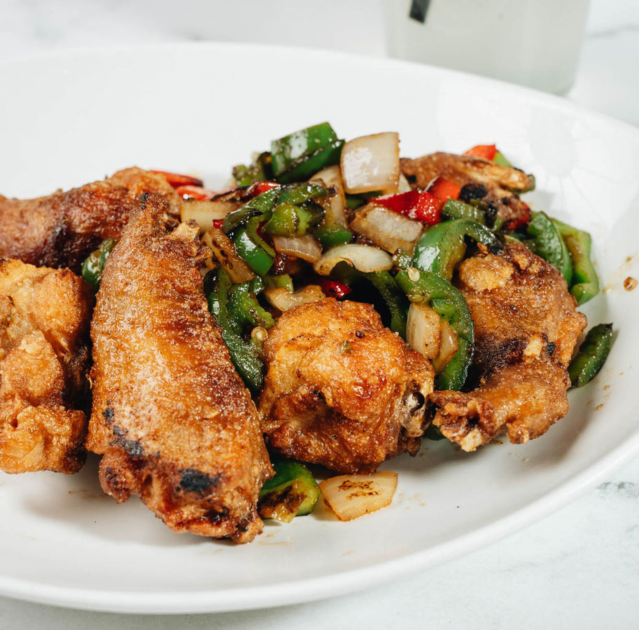 `Crispy fried chicken with stir-fried peppers and onions on a white plate`