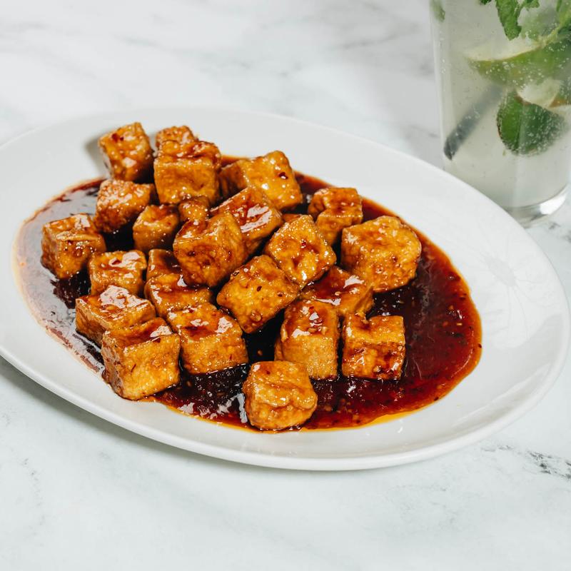 Spicy glazed tofu cubes in red sauce on an oval white plate