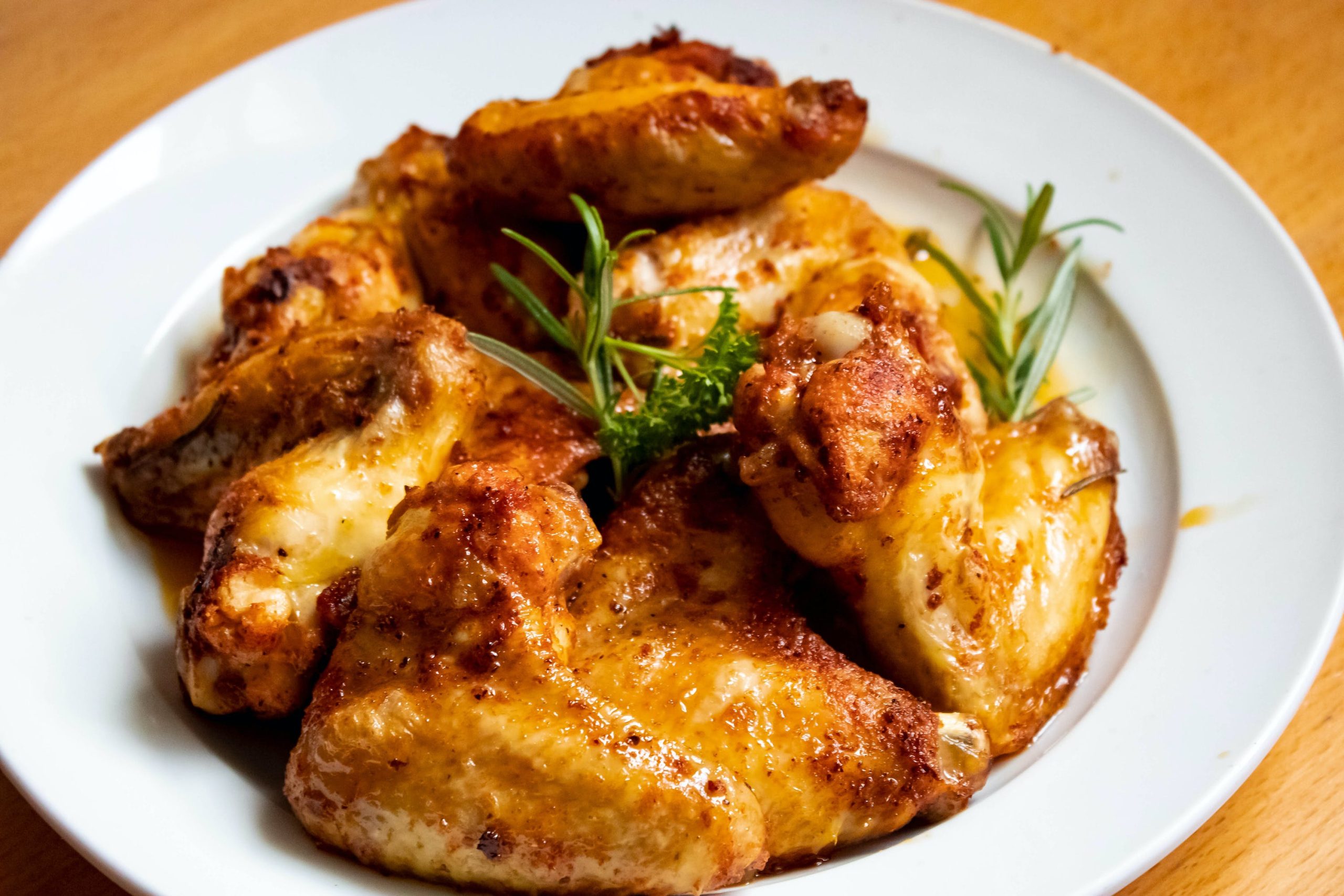 Golden roasted chicken wings with rosemary garnish on a white plate at Wing Express, a American restaurant in Deland