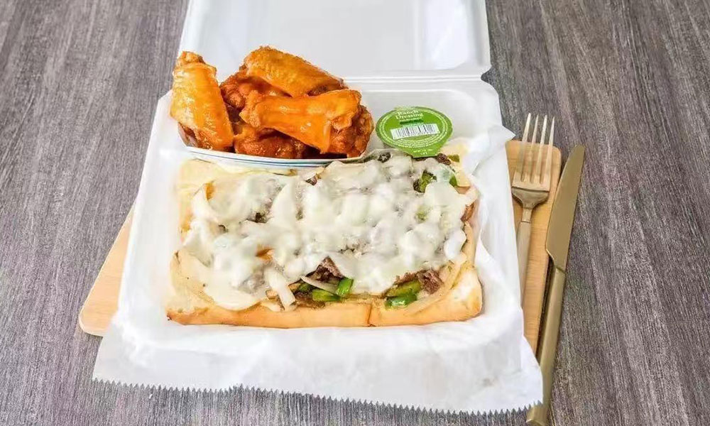 Takeout meal: cheesesteak sandwich with buffalo wings in foam container
