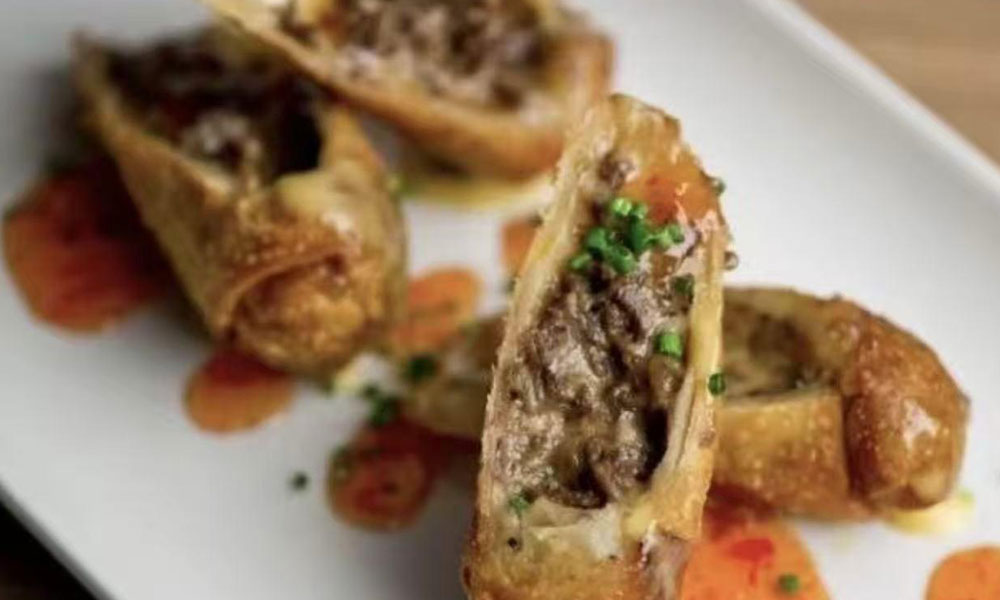 Beef-filled fried spring rolls with sauce drizzle and chive garnish