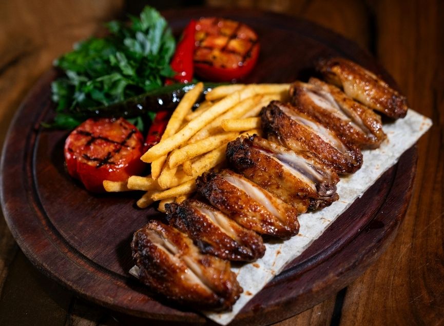 Grilled chicken wings with fries, grilled tomatoes, and greens on a wooden platter at Wing Star, a American fusion restaurant in Amsterdam
