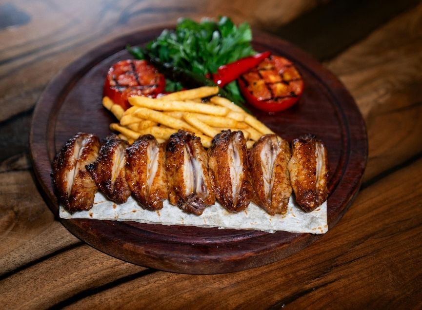 Platter of grilled chicken wings with fries, tomatoes, and fresh greens at Wing Star, a American fusion restaurant in Amsterdam