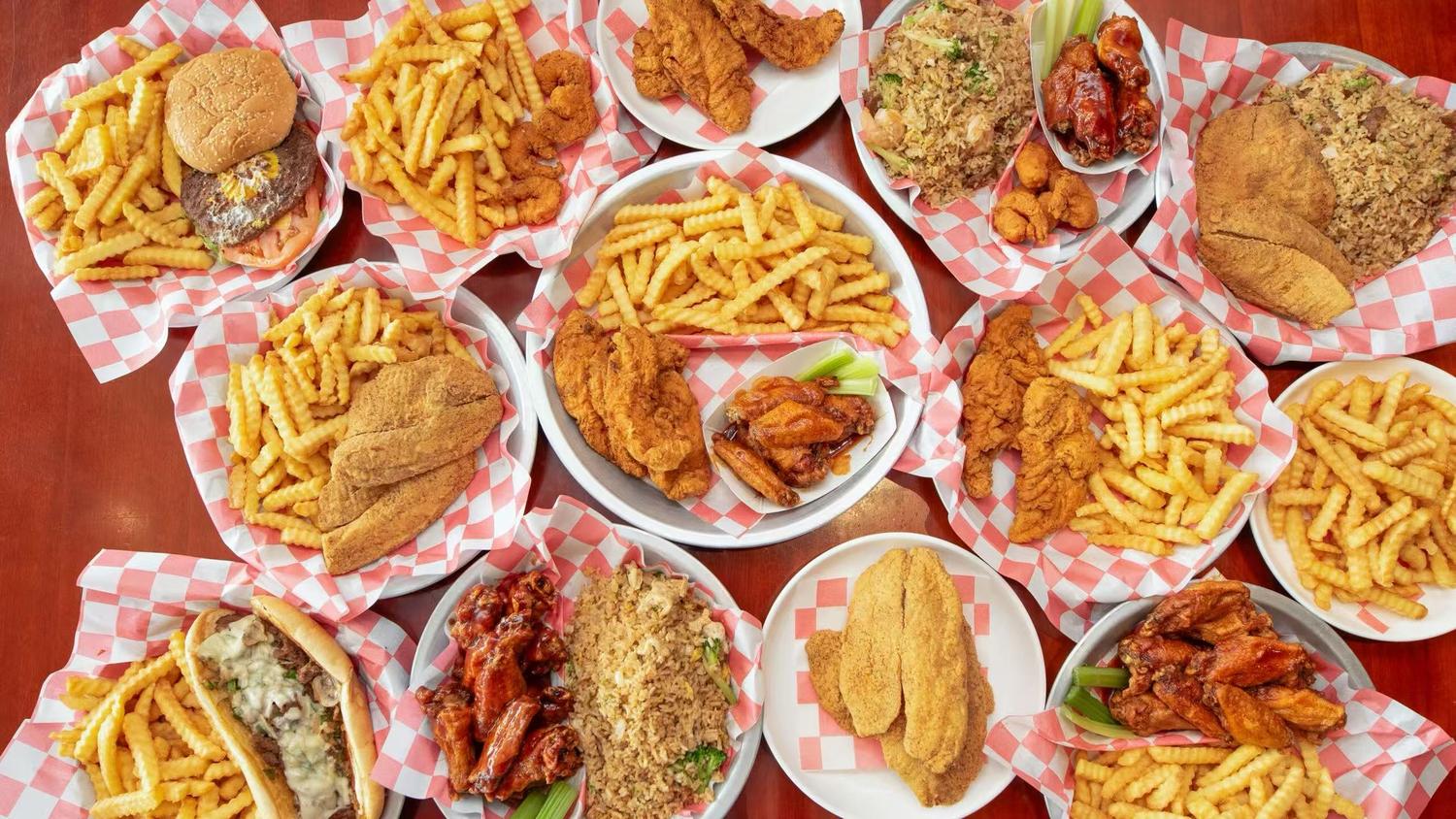 Assorted fried dishes including chicken wings, fish fillets, burgers, and fries served on checkered paper at a casual dining restaurant.