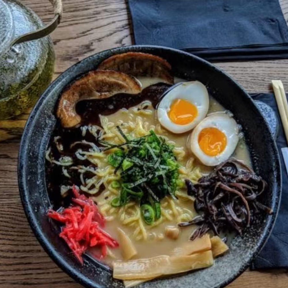 Promotional poster for Yasakani Ramen & Grill's soft opening on July 9th, 2025. Features an illustration of a bowl of ramen with noodles, egg, vegetables, and toppings, set against an orange background.