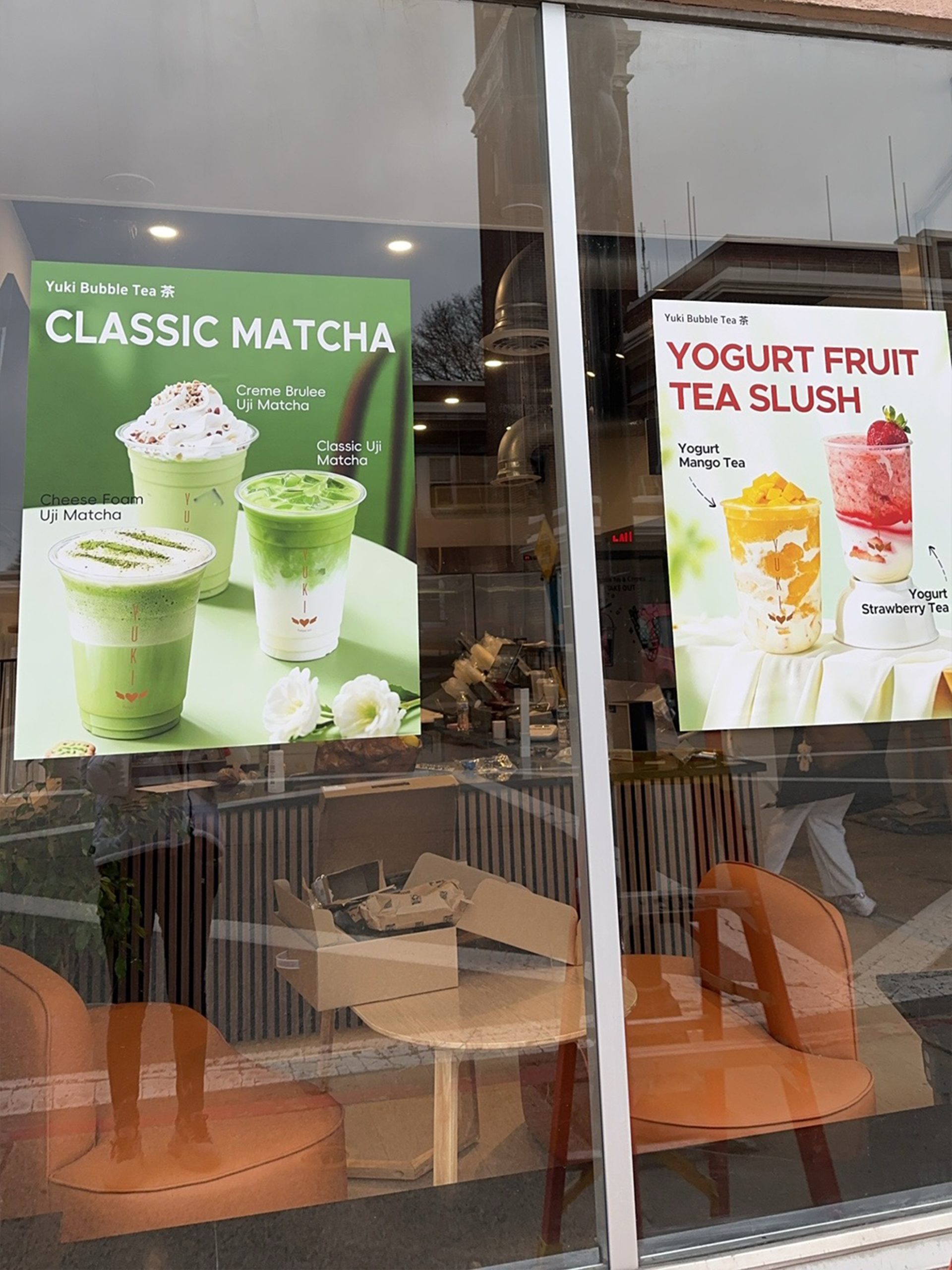 Yuki Bubble Tea storefront window with "Classic Matcha" and "Yogurt Fruit Tea Slush" posters, orange chairs inside.