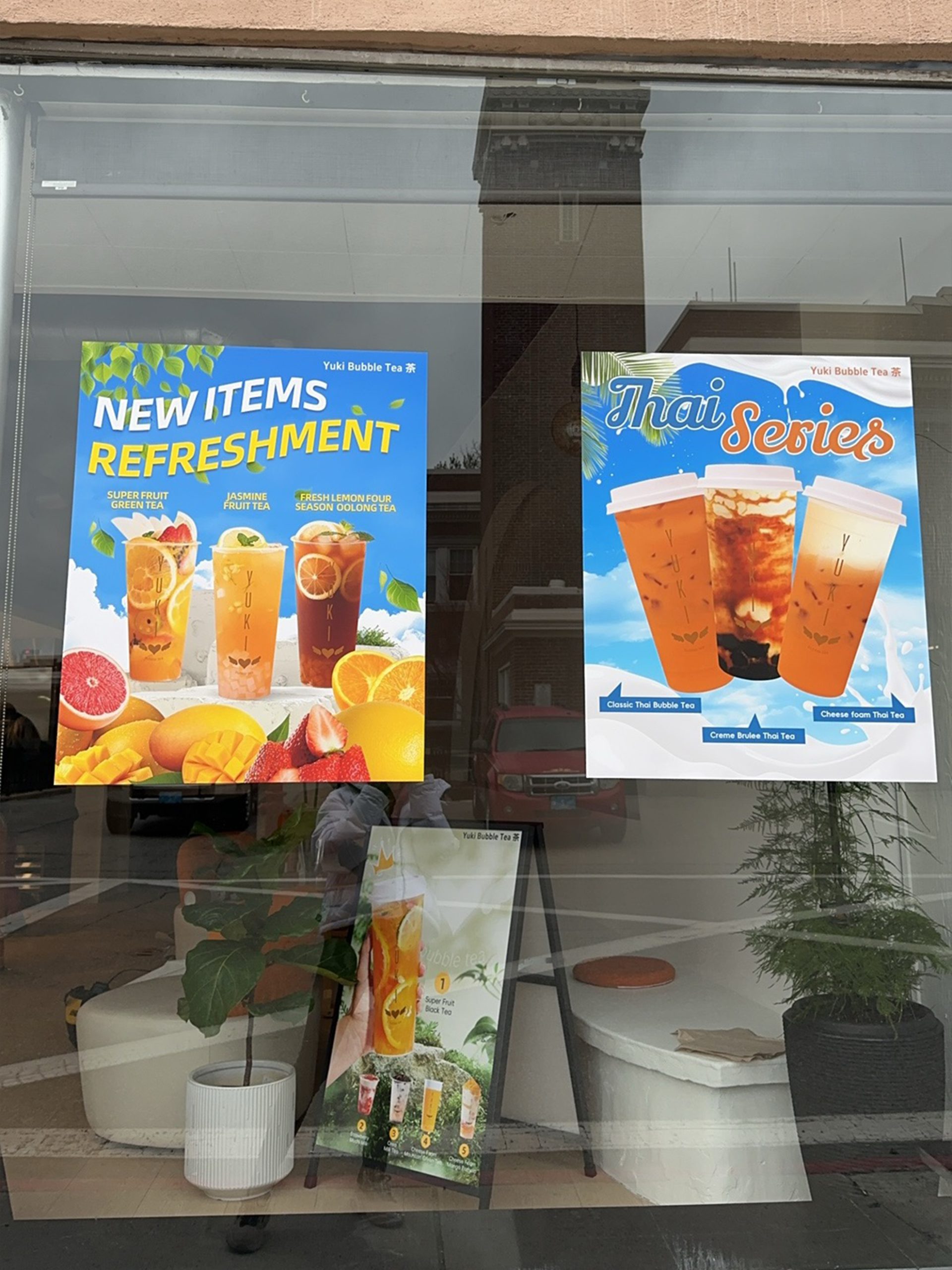 Yuki Bubble Tea window showing "New Items Refreshment" and "Thai Series" posters, indoor plants, and a sign.