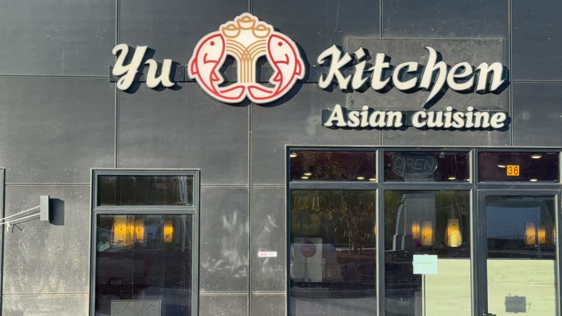 The exterior of Yu Kitchen, an Asian cuisine restaurant, featuring its logo with two fish and an "OPEN" sign in the window.