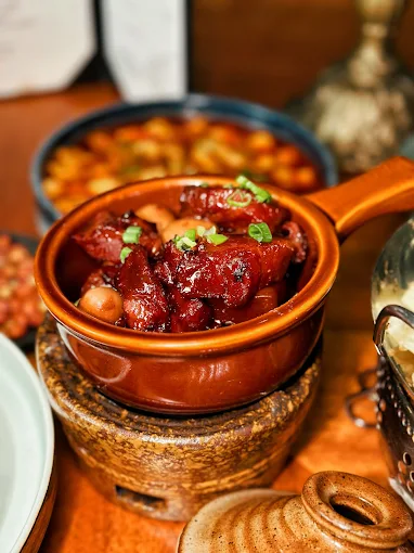 Chinese-Restaurant-Sweet-and-Sour-Pork-USA Rich, glossy braised pork belly with peanuts and green onions, served in a rustic clay pot on a wooden table.