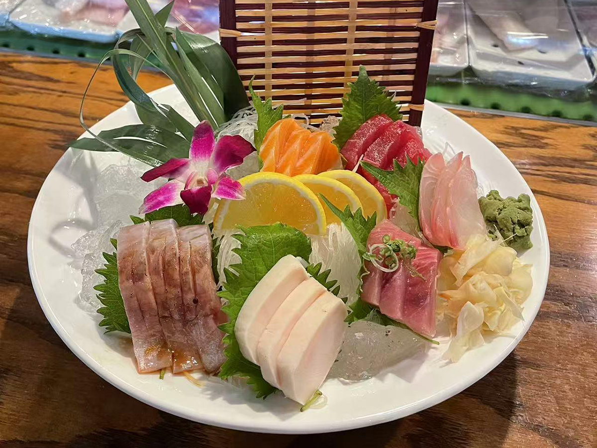 A plate of assorted sashimi including different types of raw fish, placed on ice and garnished with lemon slices, leaves, and a flower at Yume Hibachi Steak and Sushi，a Japanese Restaurant in Unionville