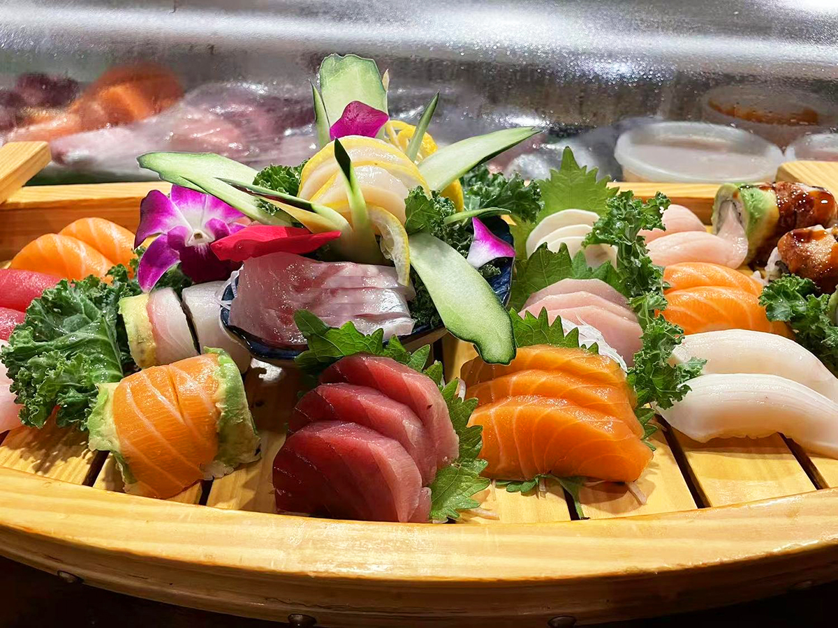 A large bamboo platter filled with an assortment of sashimi and sushi, decorated with flowers, cucumber slices, and greens at Yume Hibachi Steak and Sushi，a Japanese Restaurant in Unionville
