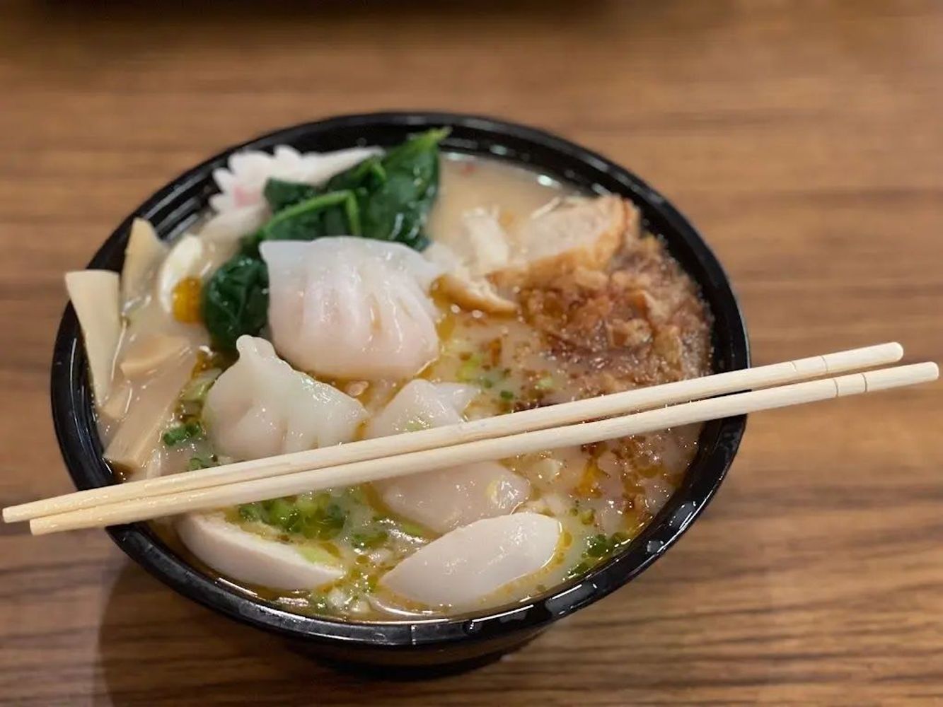 Wonton ramen bowl with dumplings, greens, bamboo shoots and chopsticks