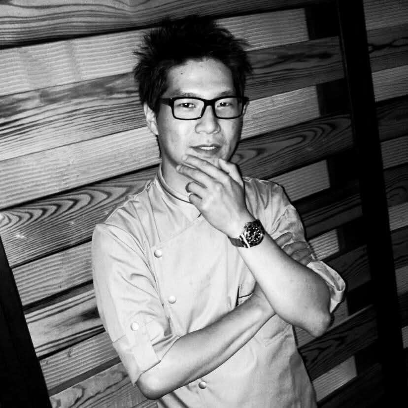 Zama-Omakase-Japanese-Restaurant-Chef-New-York Chef in uniform posing thoughtfully against a wooden wall.