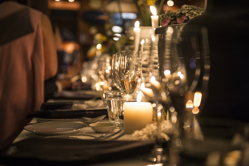 A warmly lit dinner table set with plates, glasses, and flickering candles, creating an intimate and elegant ambiance.
