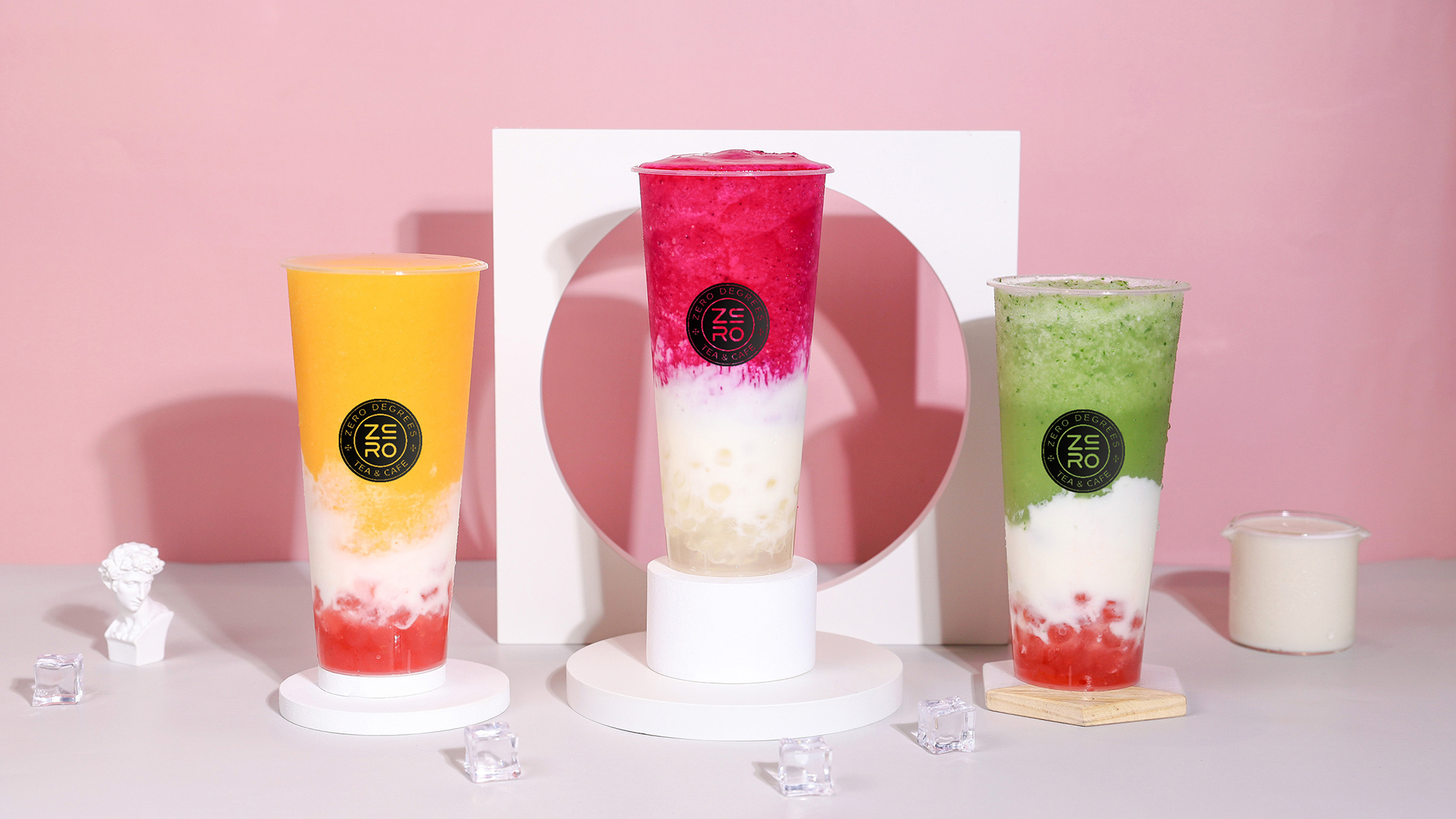 Zero-Degrees-Asian-inspired-Drink & Snack-Shop-Three-color-Layered-Specialty-Fruit-Teas-Bloomington Three cups of layered fruit teas in mango, dragon fruit, and matcha flavors, set against a pink background with a white decorative frame at Zero Degrees,a Asian-inspired Drink & Snack Shop in Bloomington