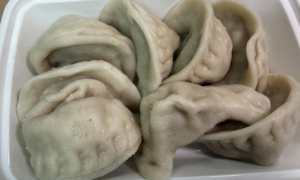 Steamed Chinese dumplings in a white takeout container, hand-folded with pleats.