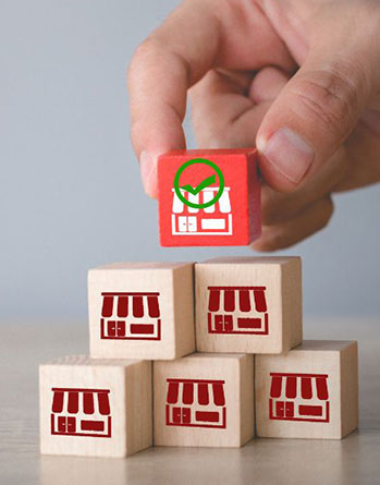 Hand holding red wooden store block with green checkmark above stacked shop logo wooden cubes on light table at Zhangliang Malatang, a Sichuan Malatang Spot in Los Angeles